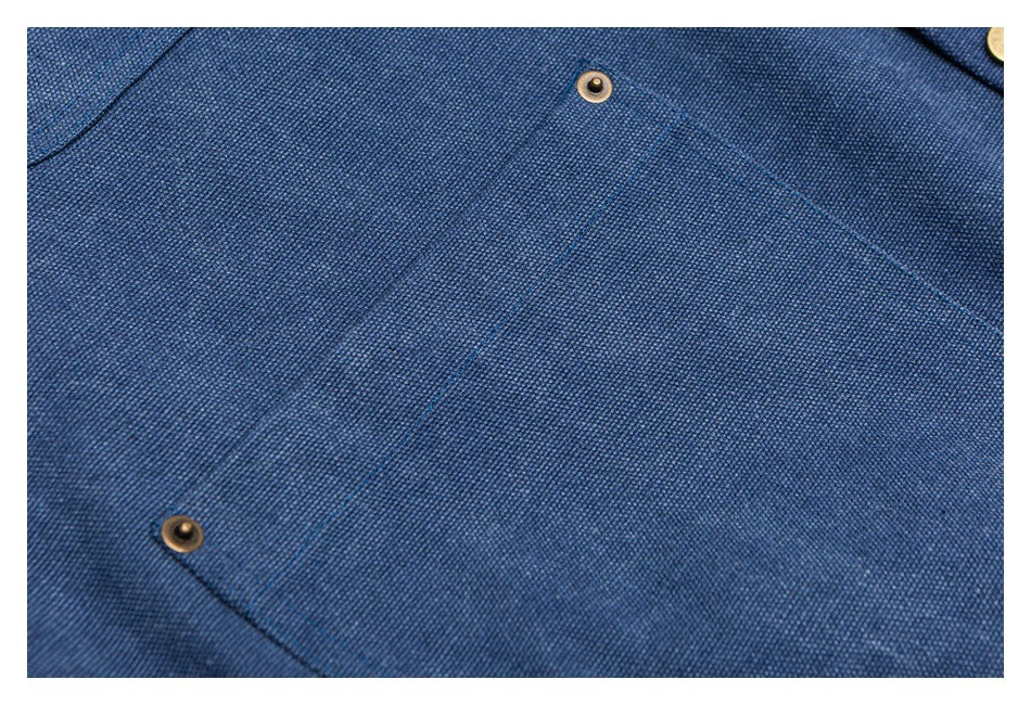 Close-up of blue woven fabric with stitched pocket edges and two brass-tone snap fasteners.