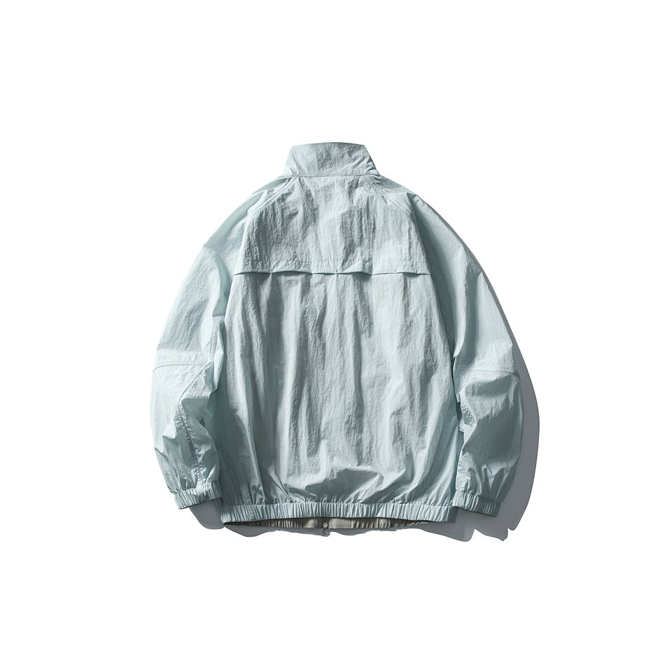 Back view of a pale blue jacket laid flat, with a stand collar, back yoke, elastic cuffs and hem.