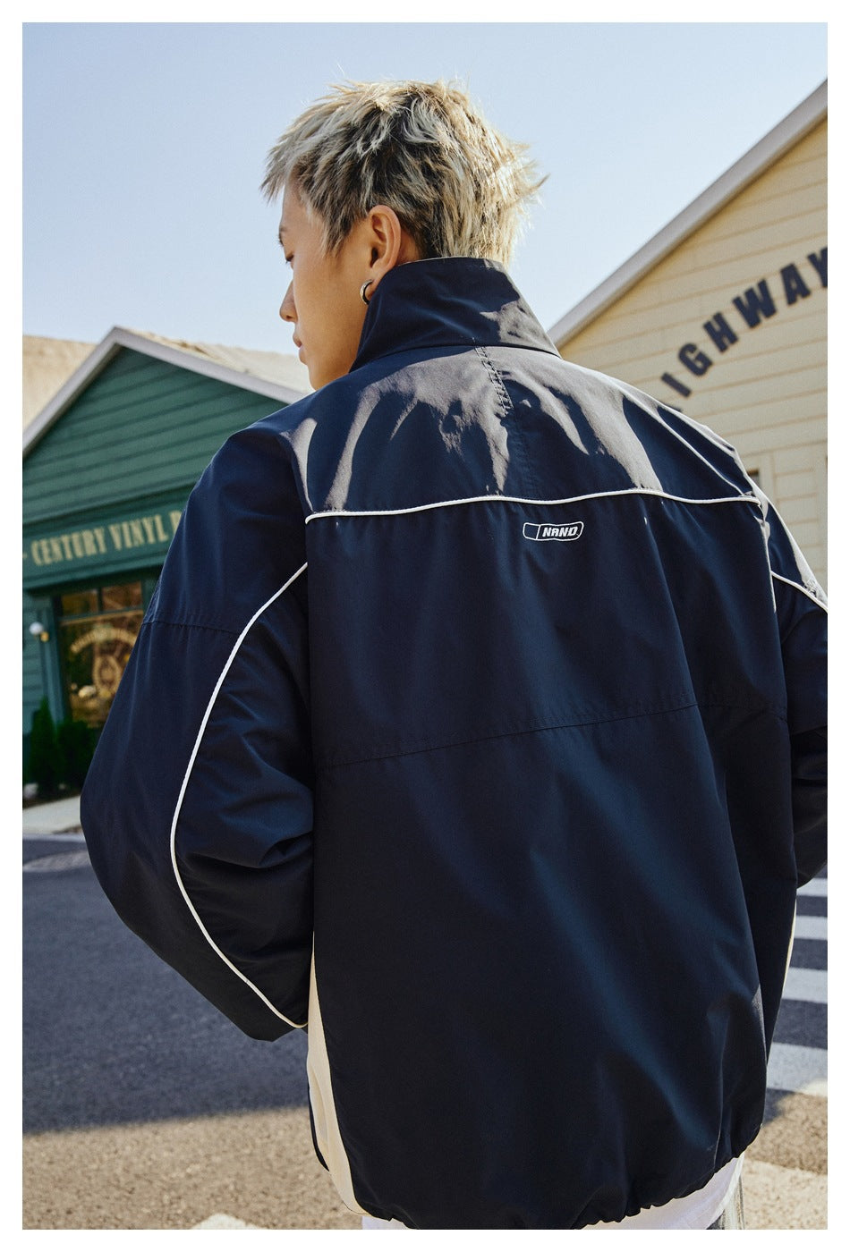 Back view of a model wearing a navy jacket with white piping and a light contrasting side panel.
