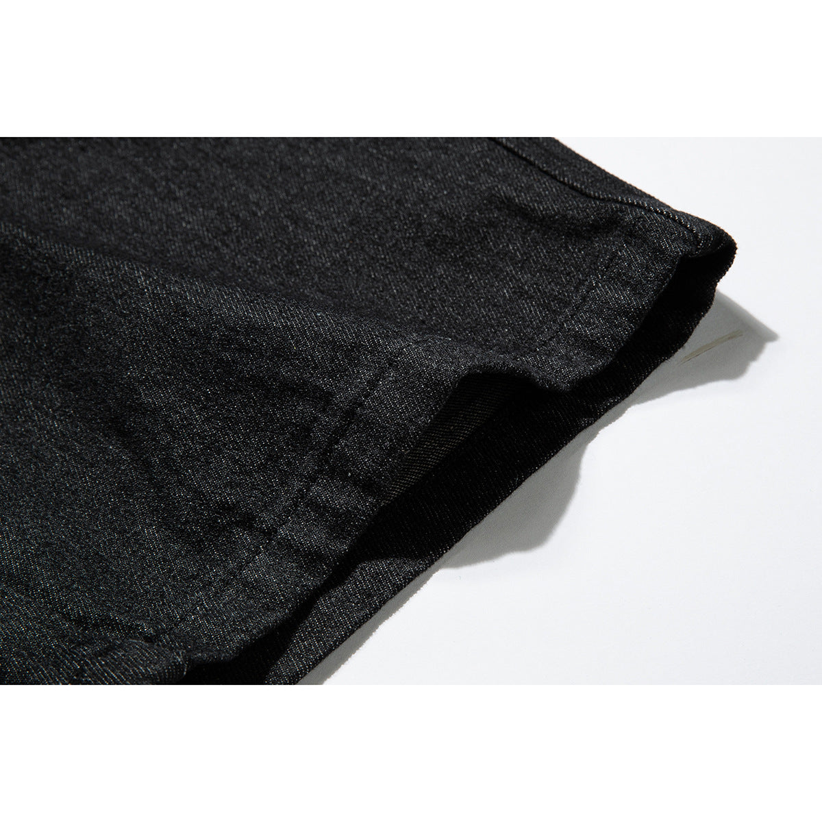 Close-up of the folded hem and stitching on black denim against a white background.