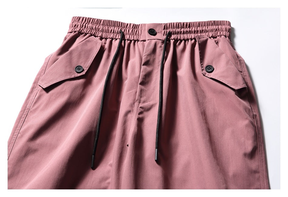 Close-up of dusty rose pants showing the elastic waist, black drawstrings, button closure, and flap pockets.