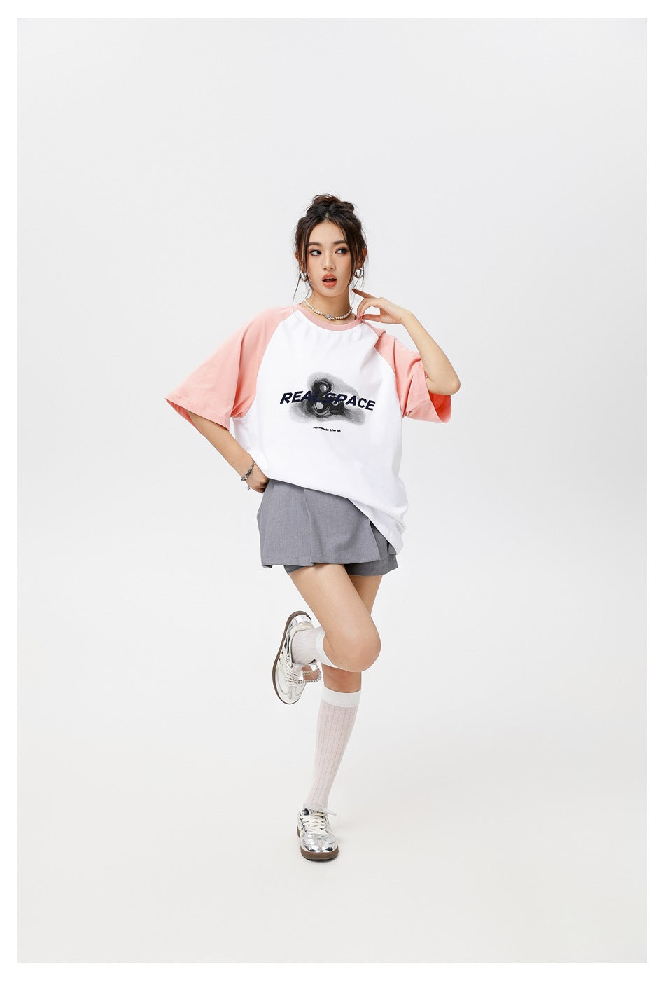 Model in the oversized pink and white raglan T-shirt with gray shorts, posing with one knee raised
