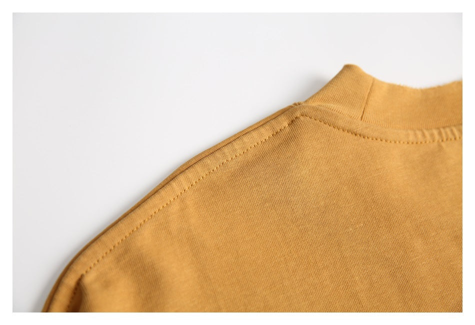 Close-up of the ochre T-shirt shoulder seam and ribbed crew neckline on a white background.