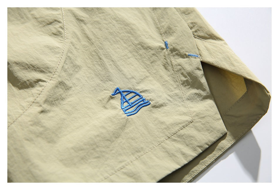 Close-up of blue sailboat embroidery on the pale khaki shorts, showing the stitched hem and side opening.