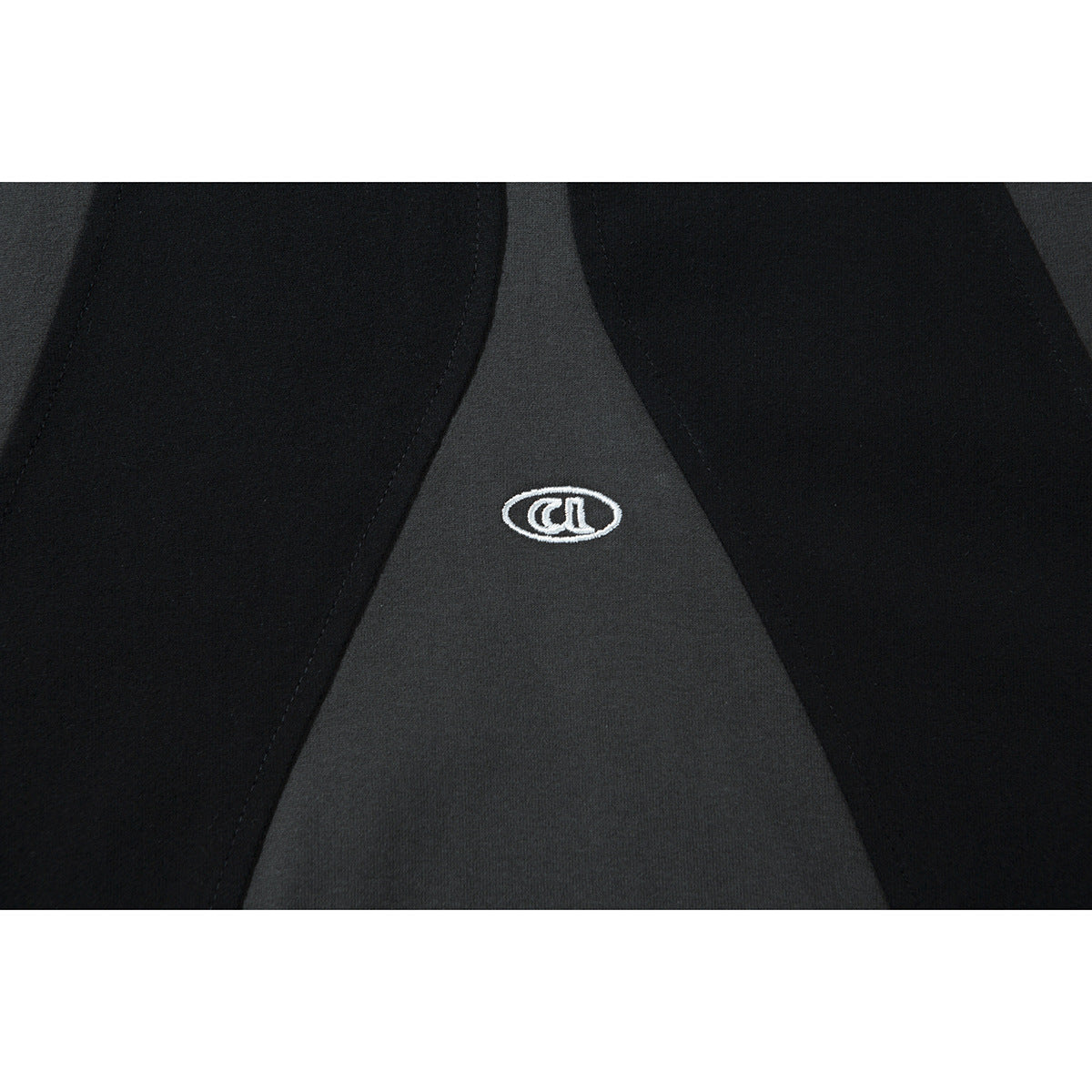 Close-up of a small white oval emblem embroidered on the charcoal center panel between black sections.