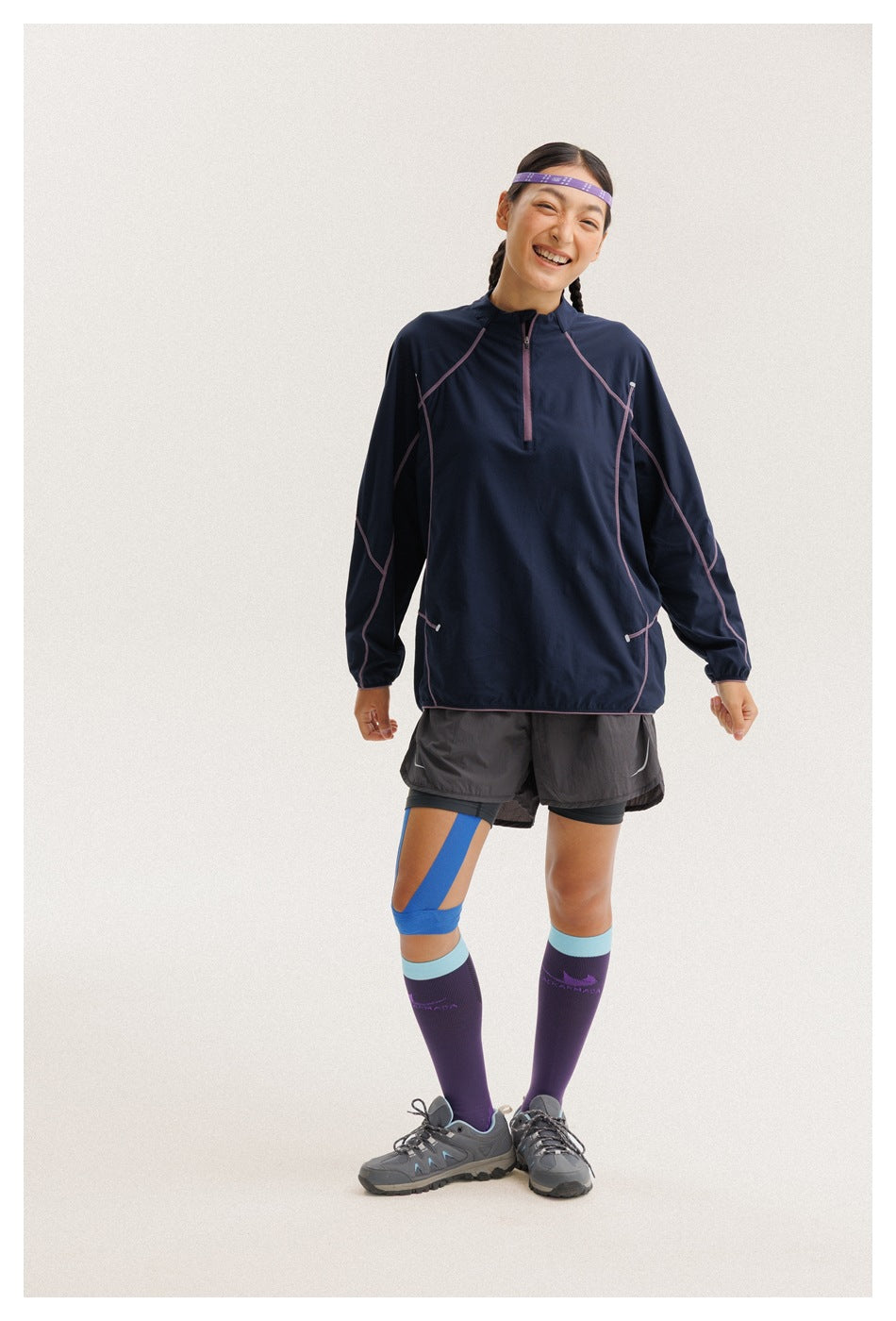 Model wearing a navy quarter-zip pullover with pink seam detailing and gray running shorts, shown from the front.