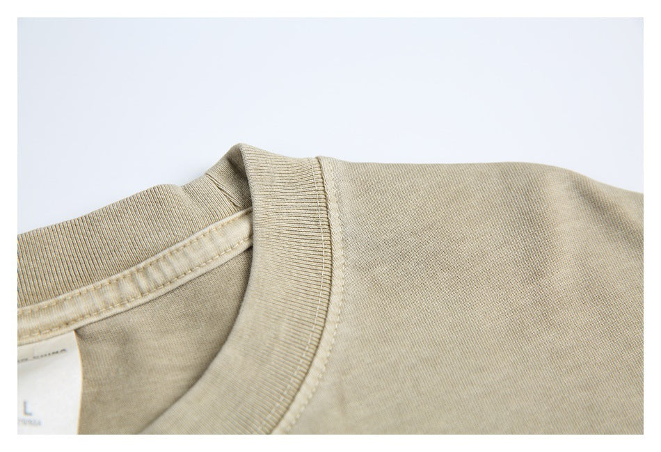 Close-up of the ribbed crew neckline and shoulder seam on a sand-beige T-shirt.