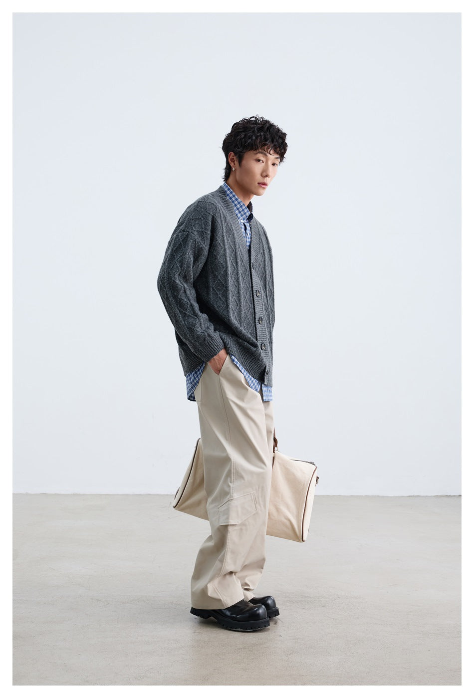 Model wearing a charcoal gray cable-knit button cardigan over a blue checked shirt and beige wide-leg trousers.
