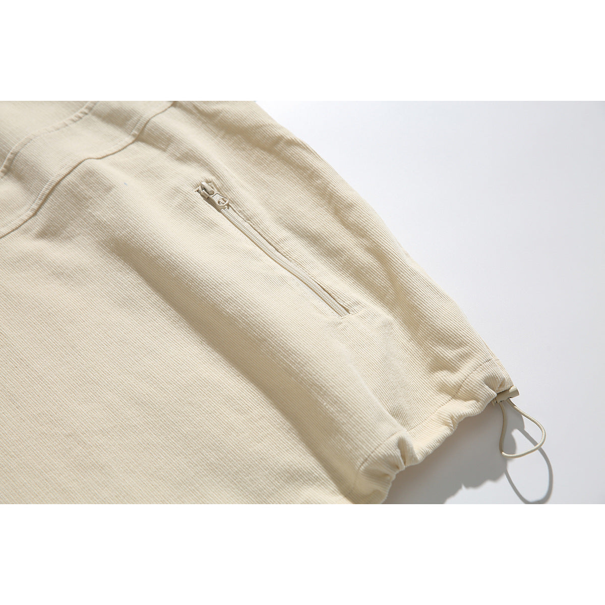Close-up of the cream jacket's sleeve, showing a zip pocket, gathered cuff, and adjustable cord.