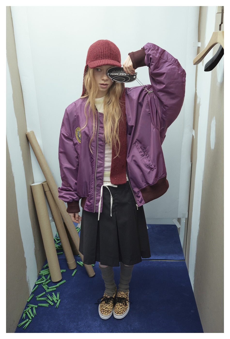 Front view of a model in a purple zip-front bomber jacket with a round chest patch and dark ribbed trim.