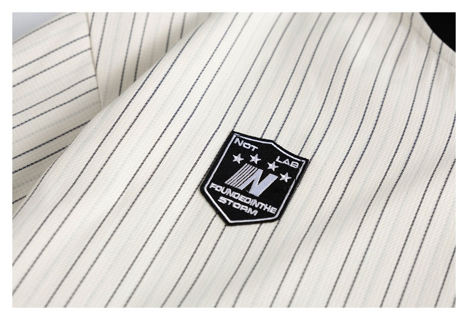 Close-up of a black shield-shaped embroidered patch on ivory fabric with thin dark pinstripes.
