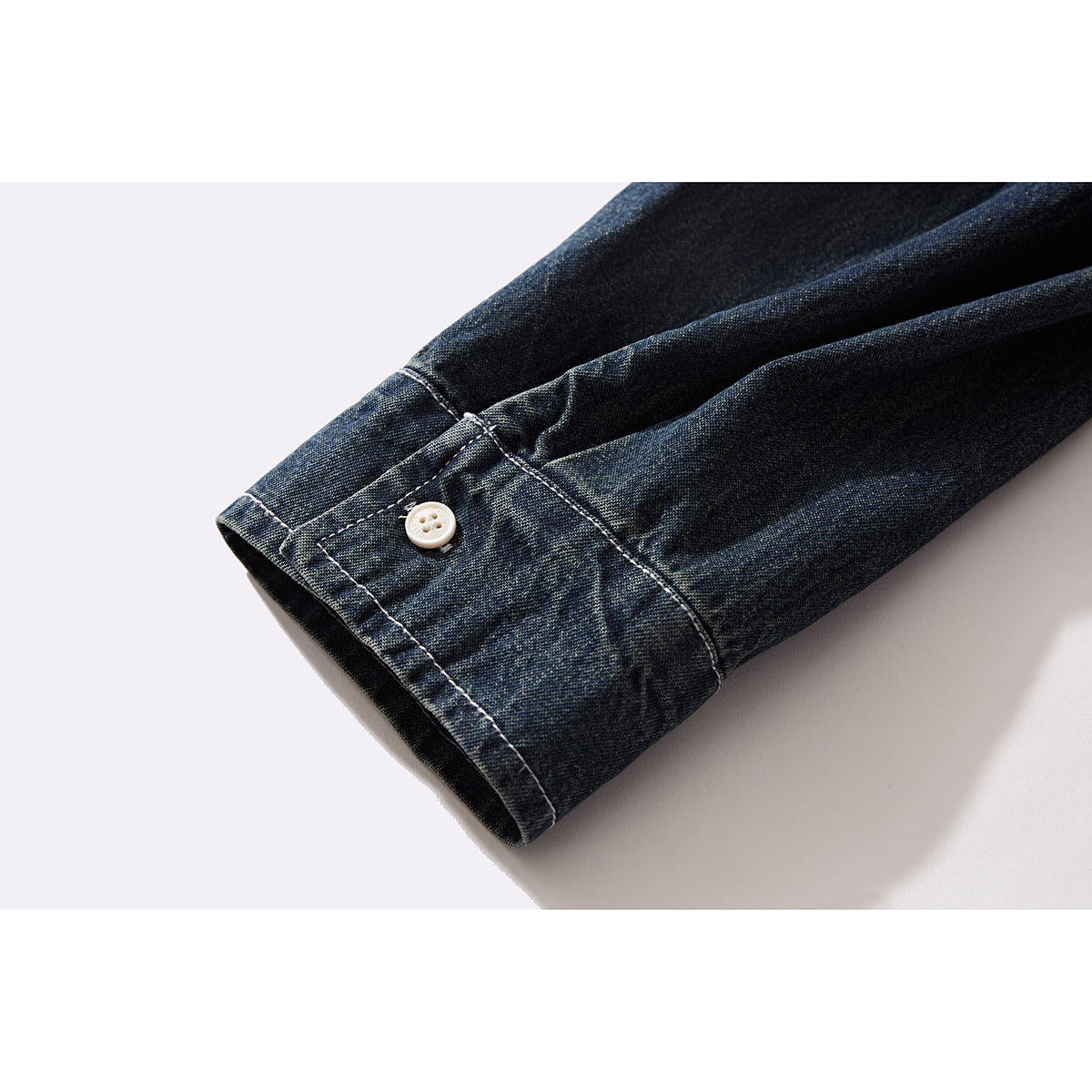 Close-up of a dark indigo denim shirt sleeve cuff with a white button and contrast stitching.