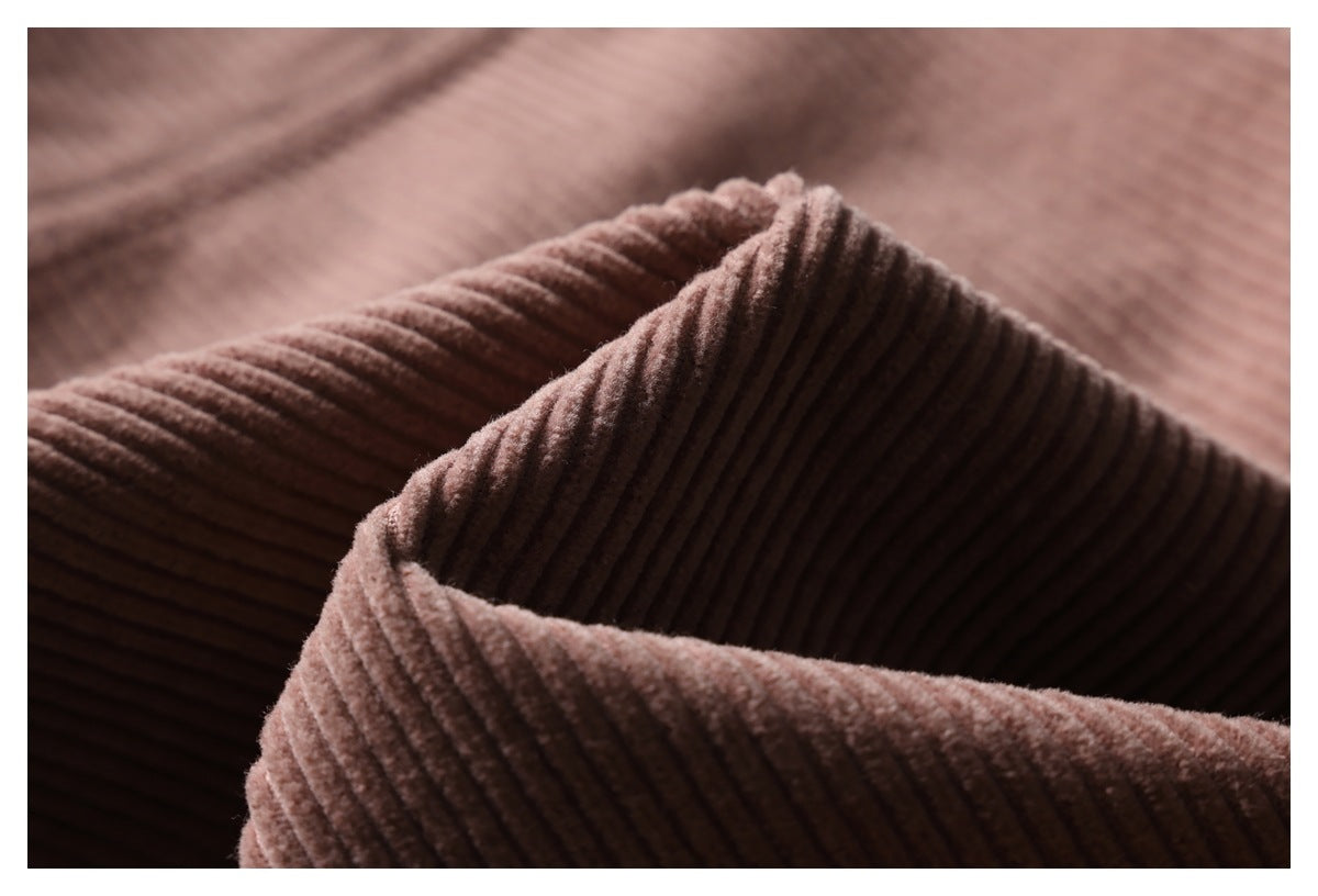 Macro view of the raised ribs and folded edge of dusty mauve-brown trouser fabric.
