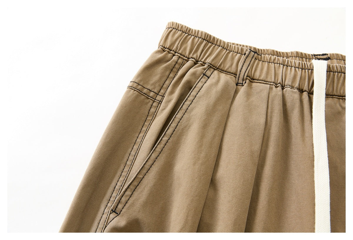 Close-up of tan pants with an elastic waistband, belt loops, slanted pocket, and white drawstring.