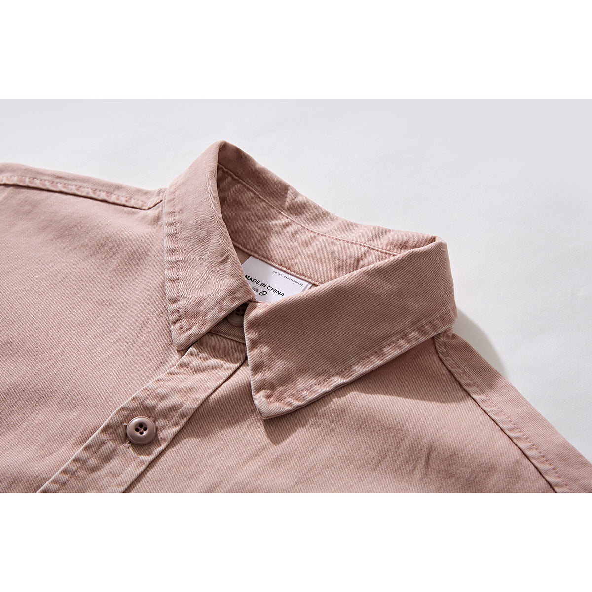 Close-up of a dusty pink shirt collar, placket, and button; an inner label is visible.