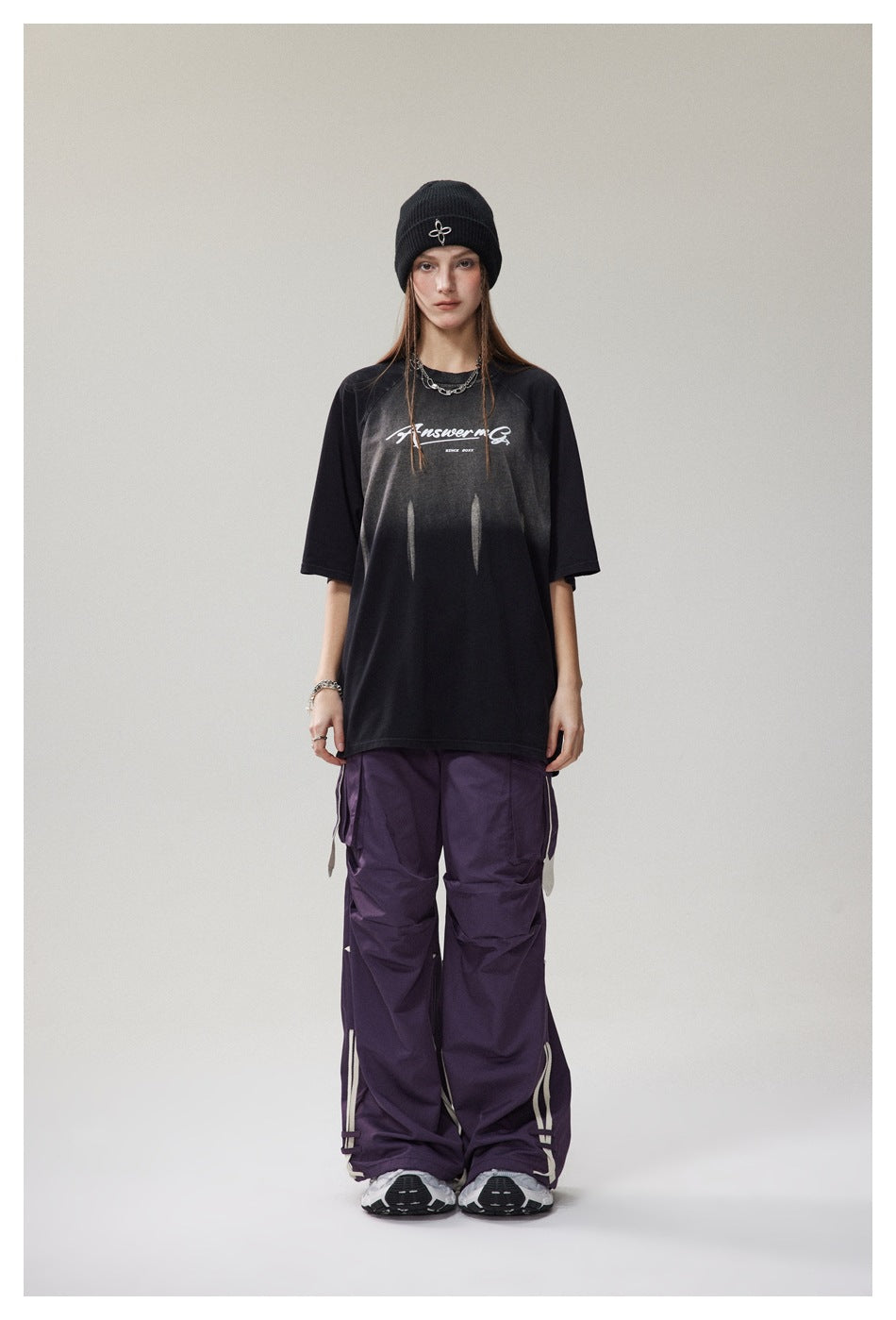 Full-length front view of a model wearing an oversized black graphic T-shirt and wide purple cargo pants.