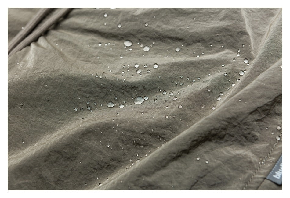 Water droplets bead on the gray-green garment; a small sewn label is partly visible at the edge.