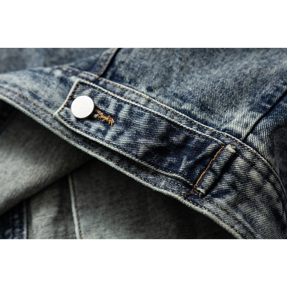 Close-up of a denim jacket sleeve tab with a silver snap and contrast stitching.