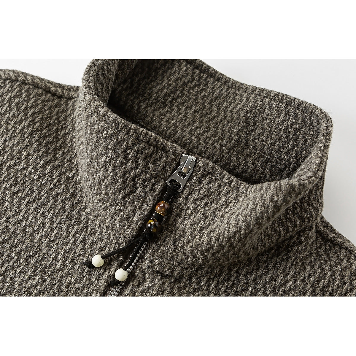 Close-up of a textured taupe-gray pullover's stand collar and short zipper with decorative bead pulls.