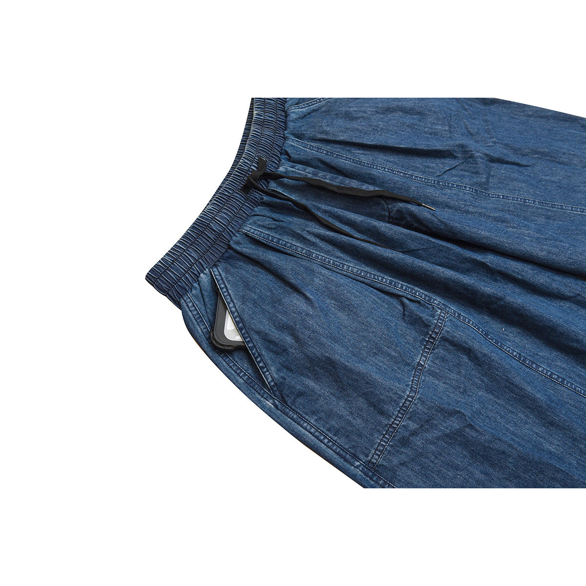 Close-up of blue denim trousers showing the elastic waistband, black drawstring, and a side pocket with a phone tucked