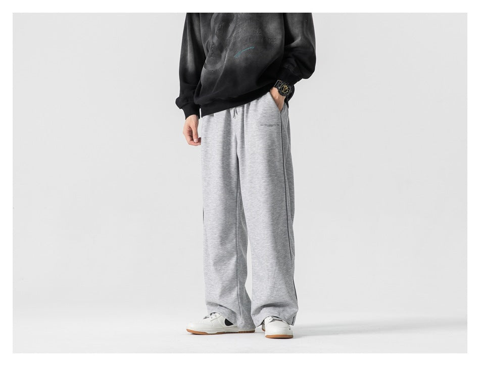 Person wearing light gray wide-leg pants with hand in pocket, black faded sweatshirt, angled view