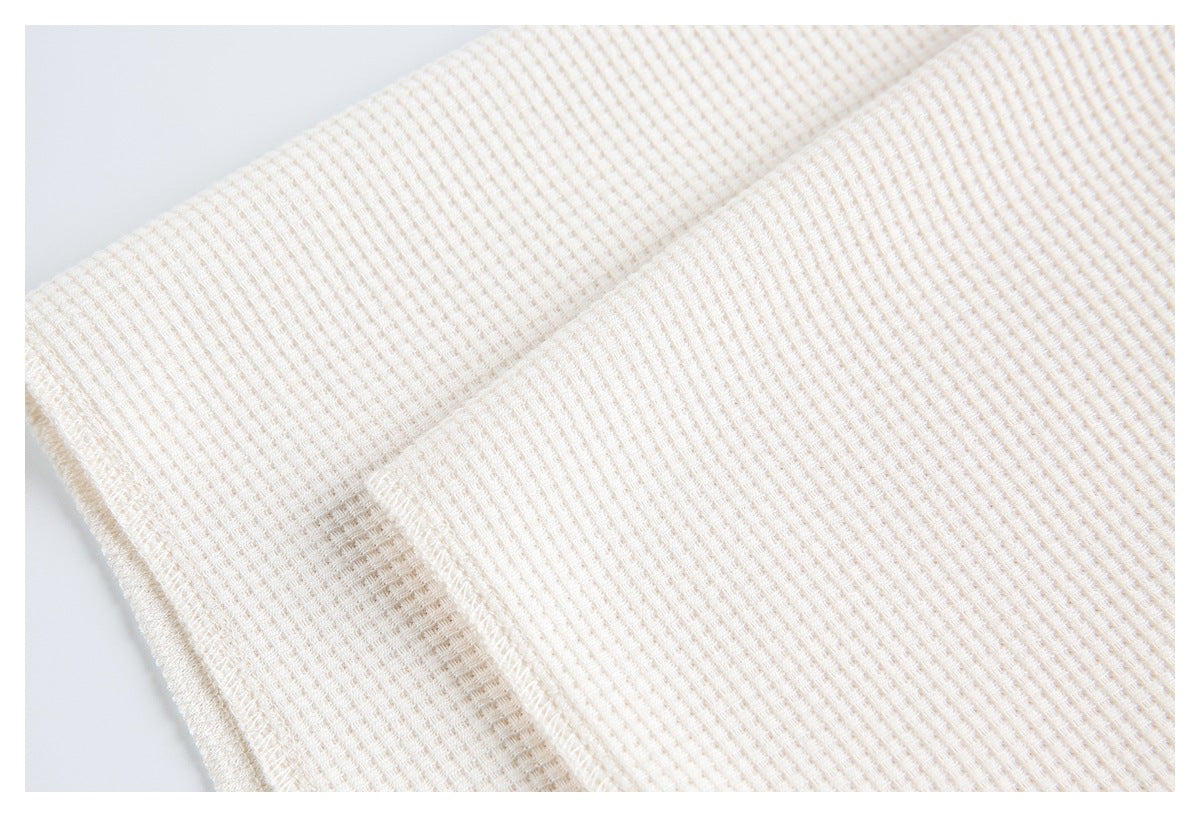 Close-up of an off-white waffle-knit garment edge with a stitched seam.
