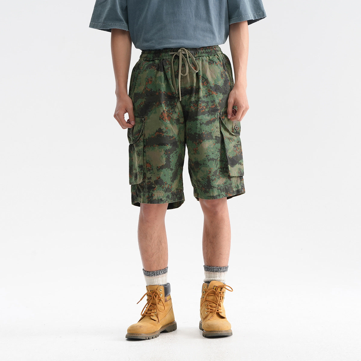 Front view of a model wearing green camouflage cargo shorts with an elastic drawstring waist and flap pockets.