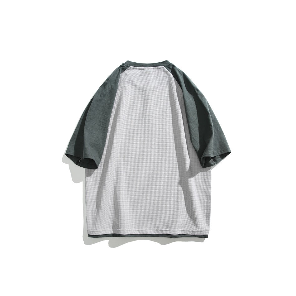 Flat lay of the back of a gray raglan shirt with dark green sleeves and matching hem trim.