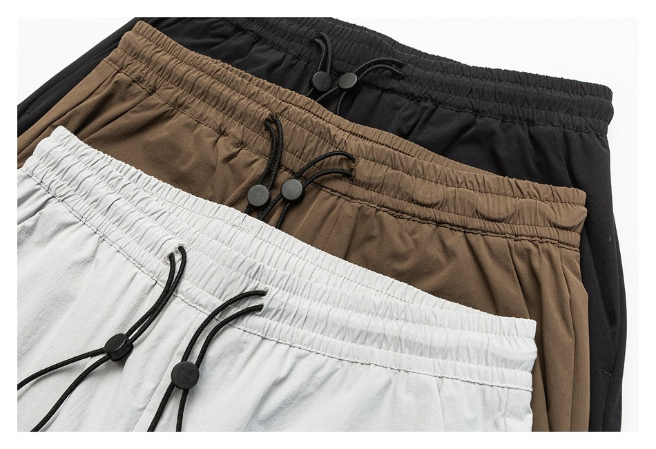 Close-up of black, brown, and light gray pants showing elastic waists with black drawcords and toggles.