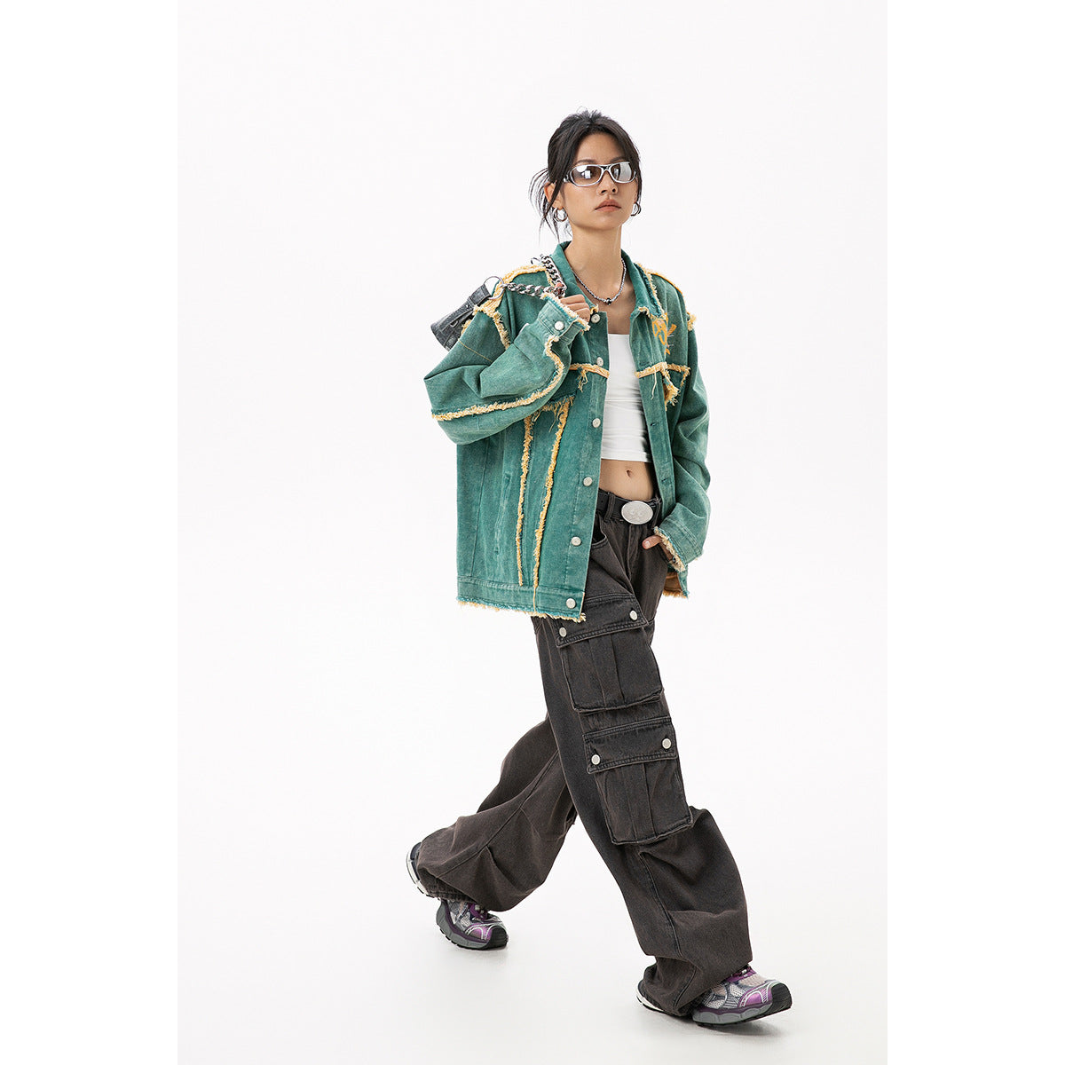 Full-length model wearing an oversized teal jacket with yellow frayed trim and black cargo pants, front view.