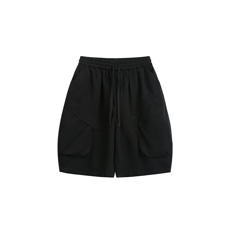 Black drawstring shorts with large patch pockets and diagonal seams, front view on white background