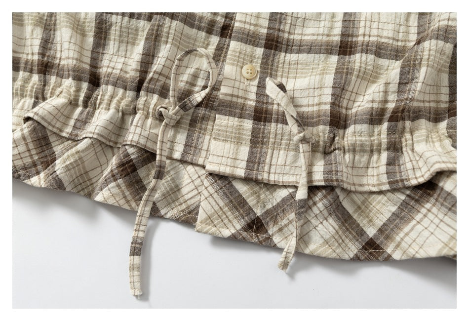 Close-up of a gathered waist with plaid drawstrings and a button on a beige and brown plaid garment.