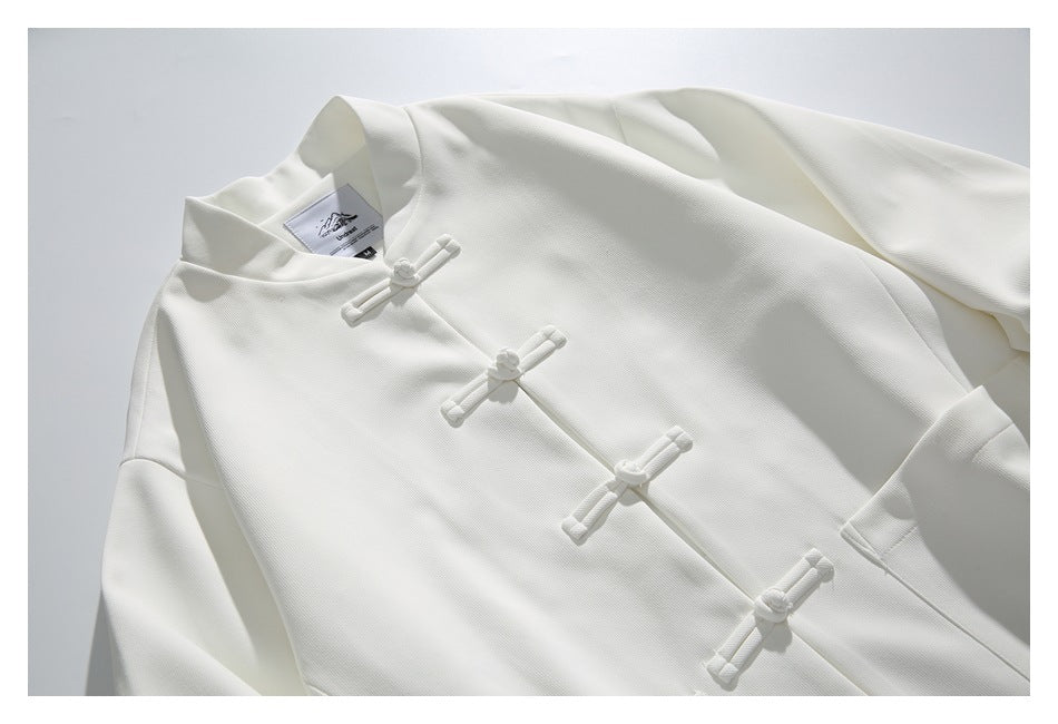 Angled close-up of a white mandarin-collar jacket with four frog closures and a visible neck label.