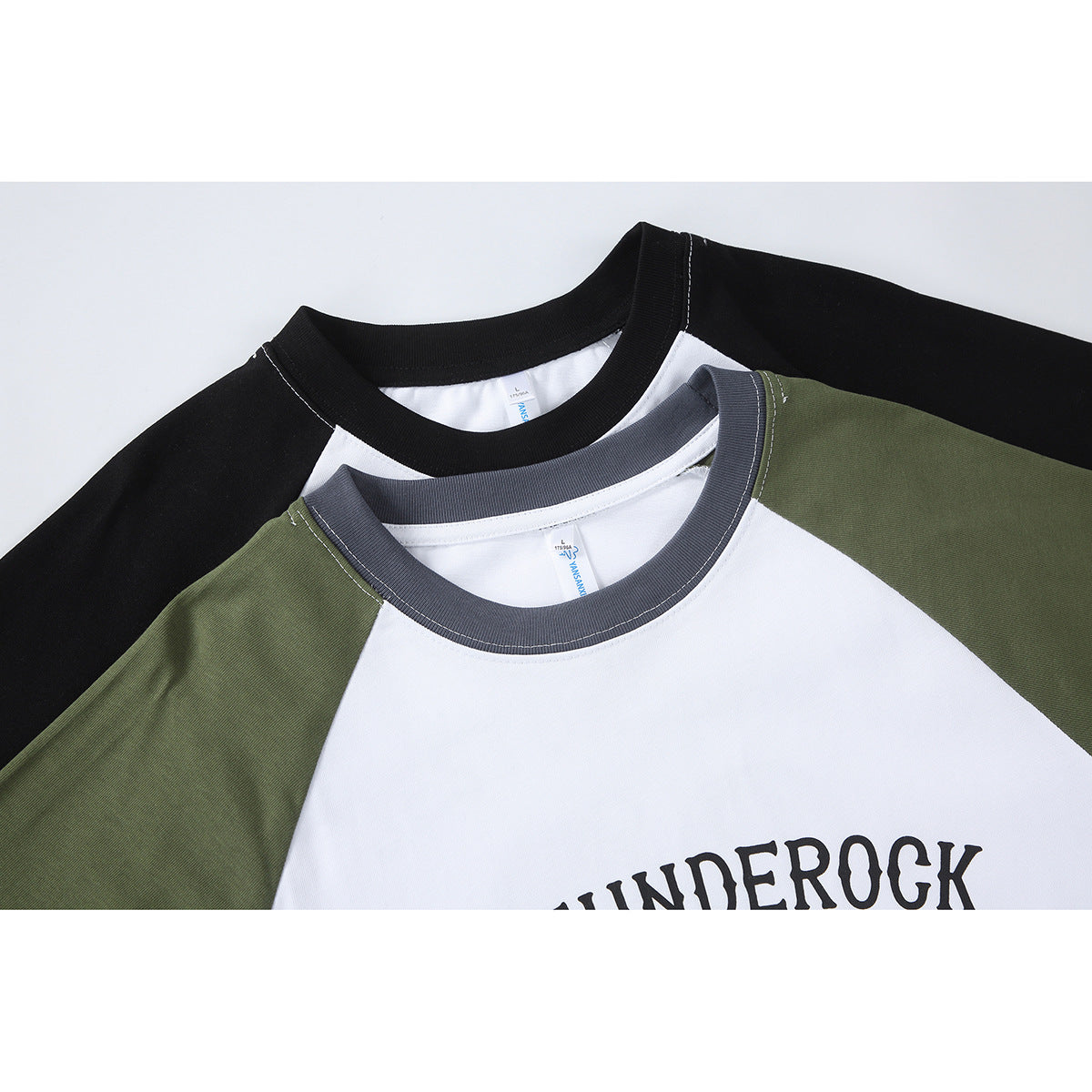 Close-up of overlapping white raglan T-shirts with black and olive sleeves and contrasting dark ribbed collars.
