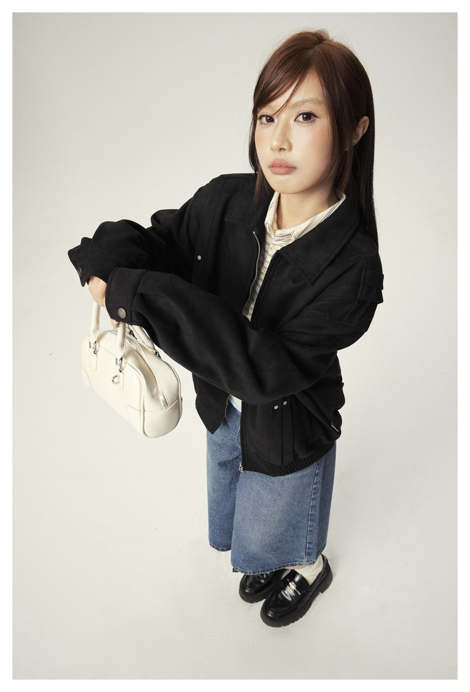Close view of a model wearing a black jacket with a pointed collar, zip front, and cuff tabs.