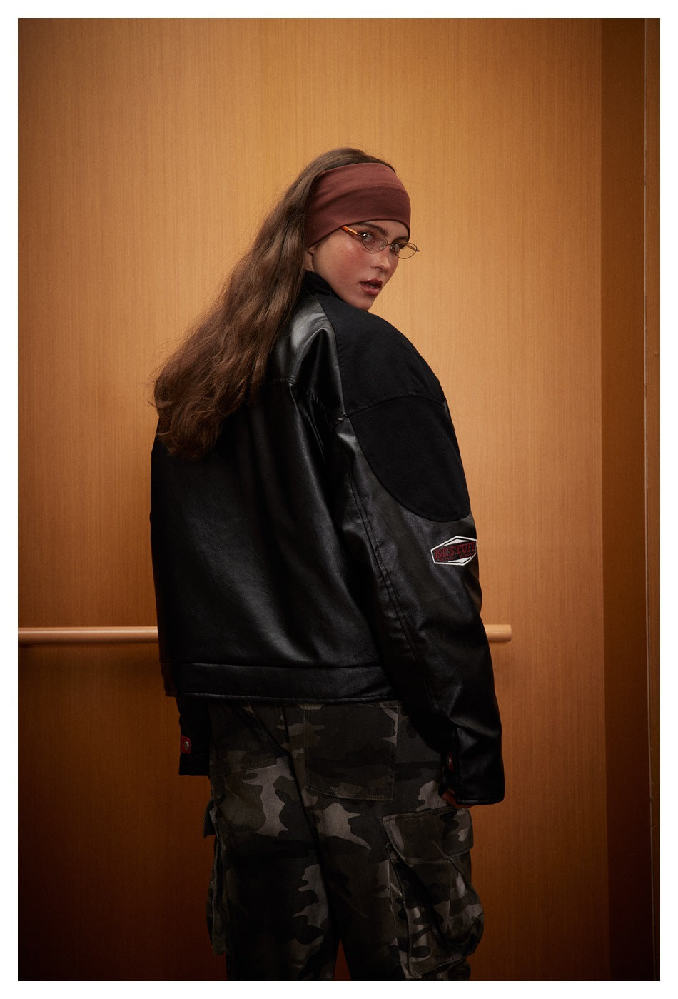 Model turning to show the back and side of a black jacket with a contrasting sleeve patch.