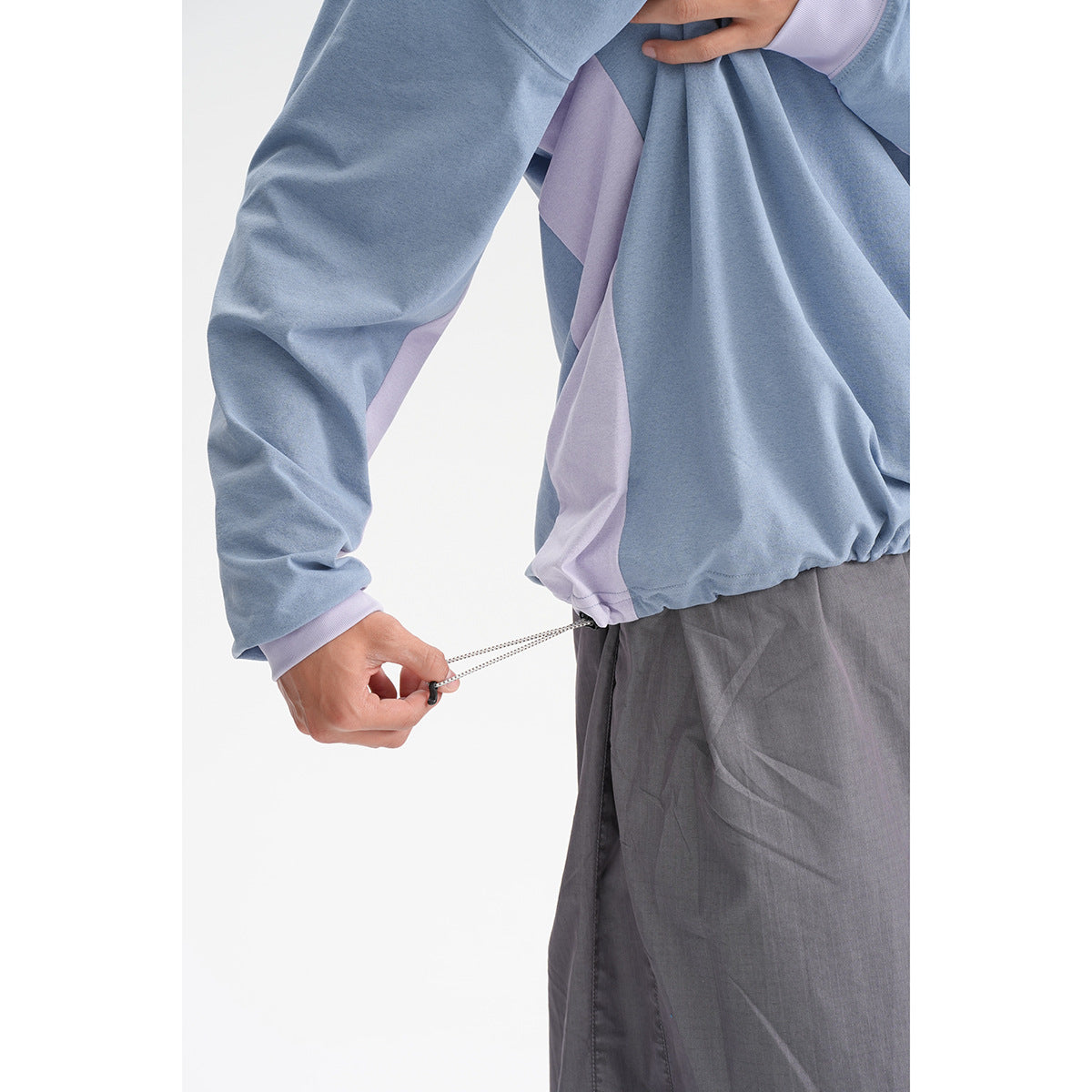 Close-up of a blue and pale-lavender color-block top with a drawcord hem above gray trousers.