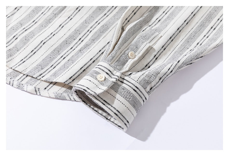 Close-up of the cream shirt's buttoned cuff and sleeve, showing the black stripe pattern.