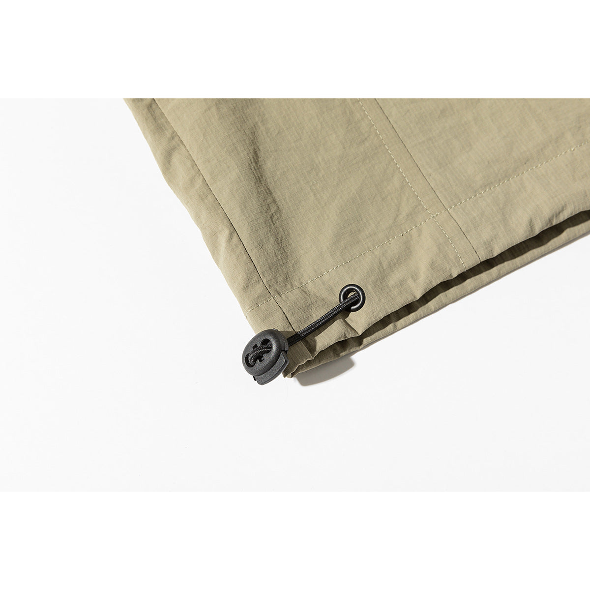 Close-up of a khaki jacket hem with a black elastic drawcord and toggle.