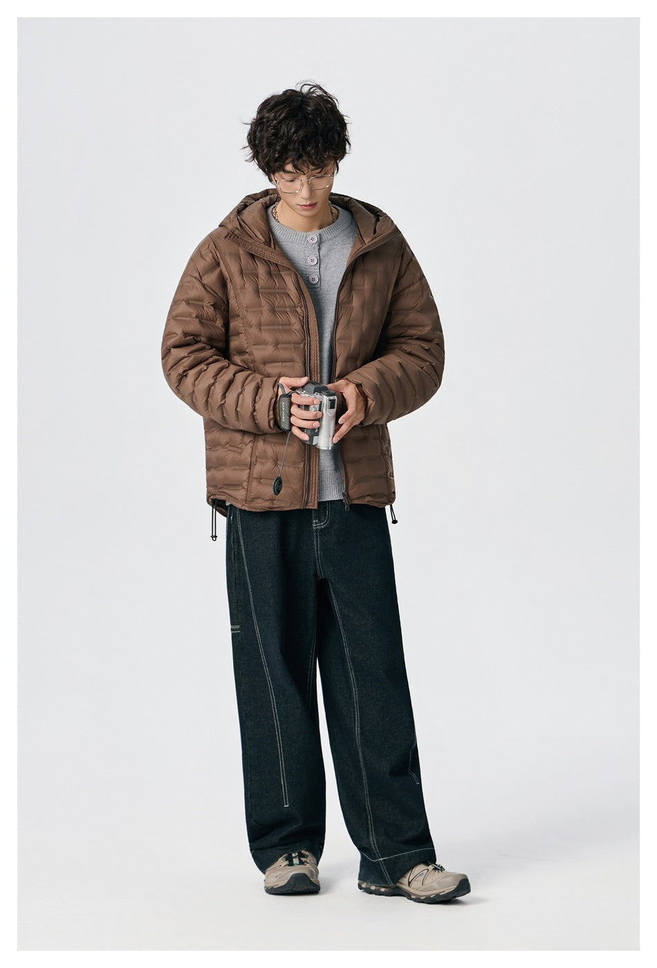 Model wearing an open brown quilted hooded jacket over a gray top with dark jeans.