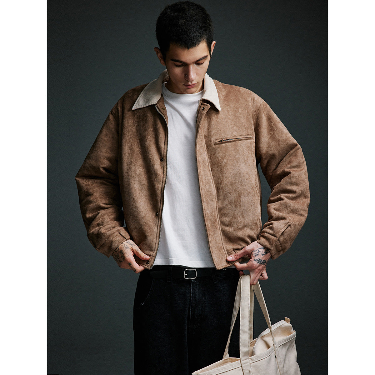 Man models a tan jacket with a cream collar, front zipper, snap placket and zip chest pocket, holding a cream tote.