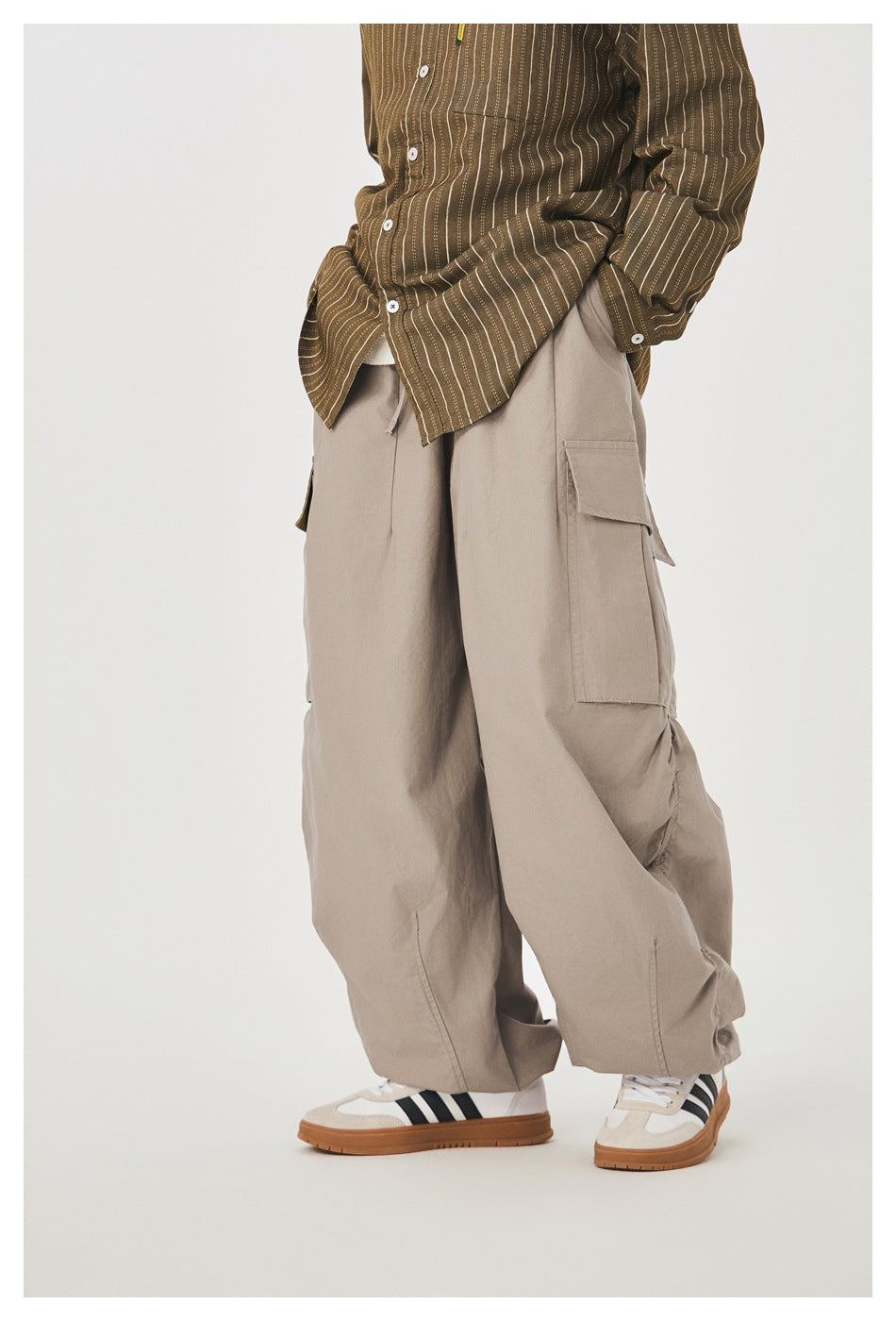 Side view of model in taupe wide-leg cargo pants with flap pocket, ruched side seam, striped shirt and sneakers