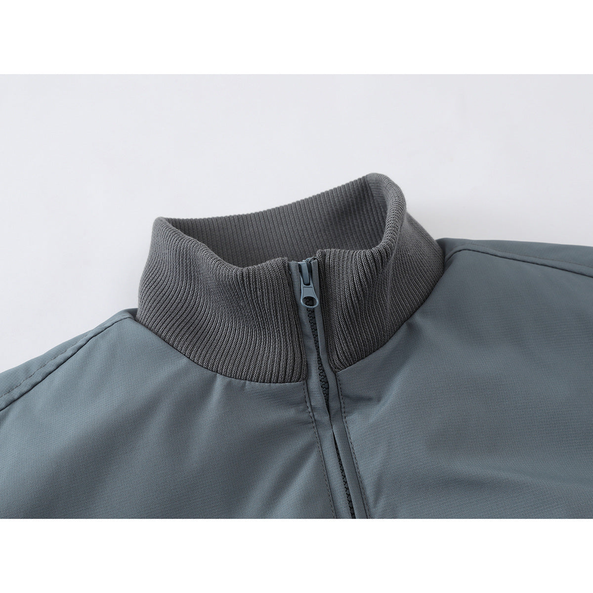 Close-up of a slate blue-gray jacket's dark ribbed stand collar and center zipper.