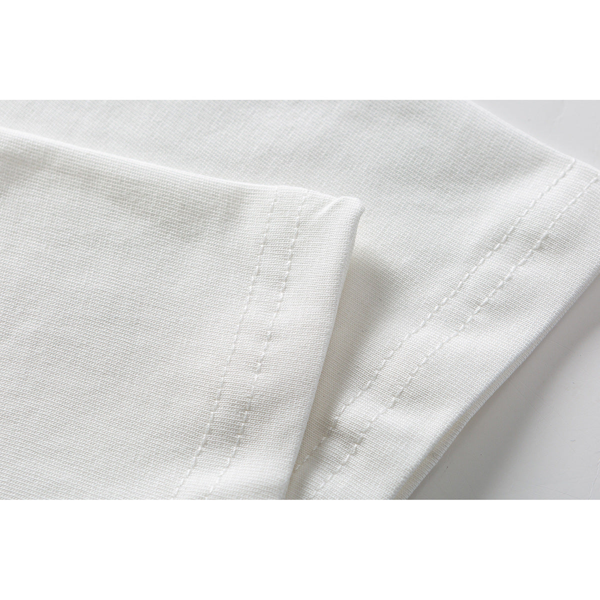 Close-up of white garment fabric showing parallel rows of stitching along a folded edge.