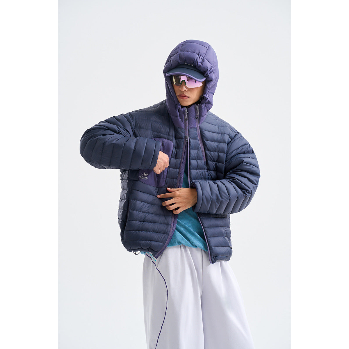 Model wearing a dark navy quilted hooded jacket with a purple hood and front pocket.
