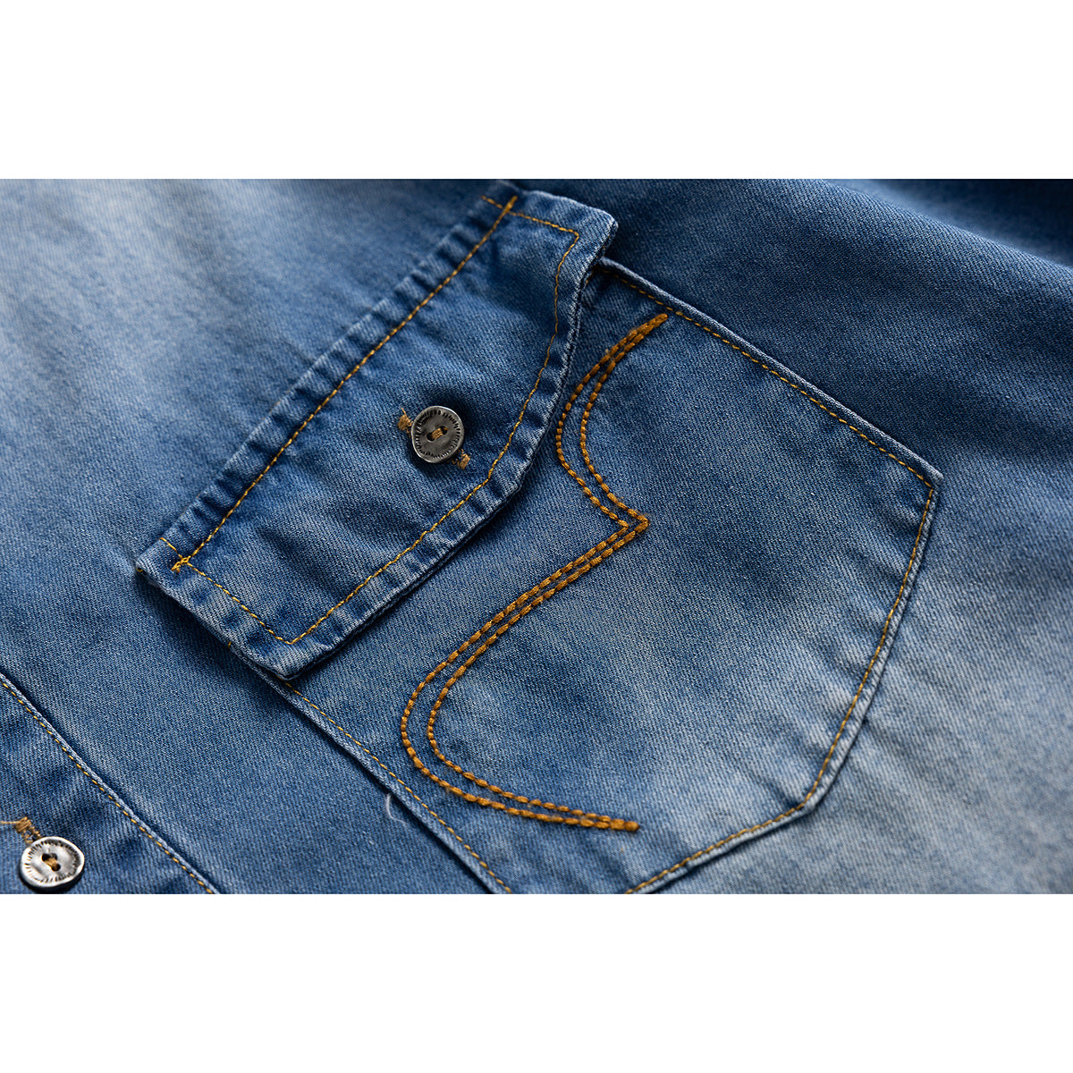 Close-up of a light blue denim shirt's buttoned chest pocket with curved contrast stitching.