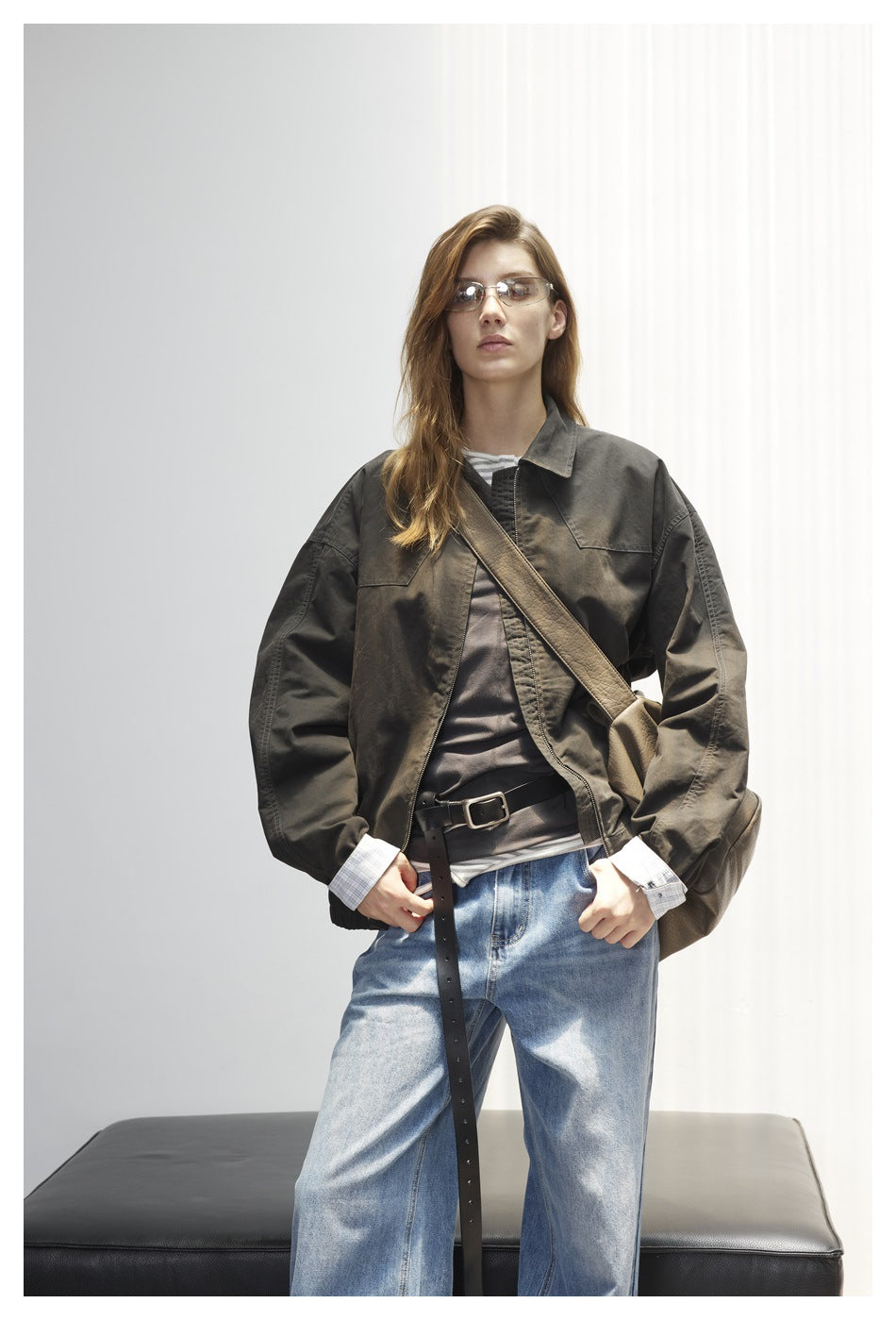 Model faces forward in a dark olive oversized jacket with chest pockets and wide sleeves, paired with blue jeans.