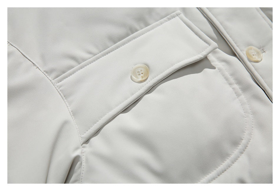 Close-up of an ivory jacket showing a buttoned pocket flap and curved pocket stitching.