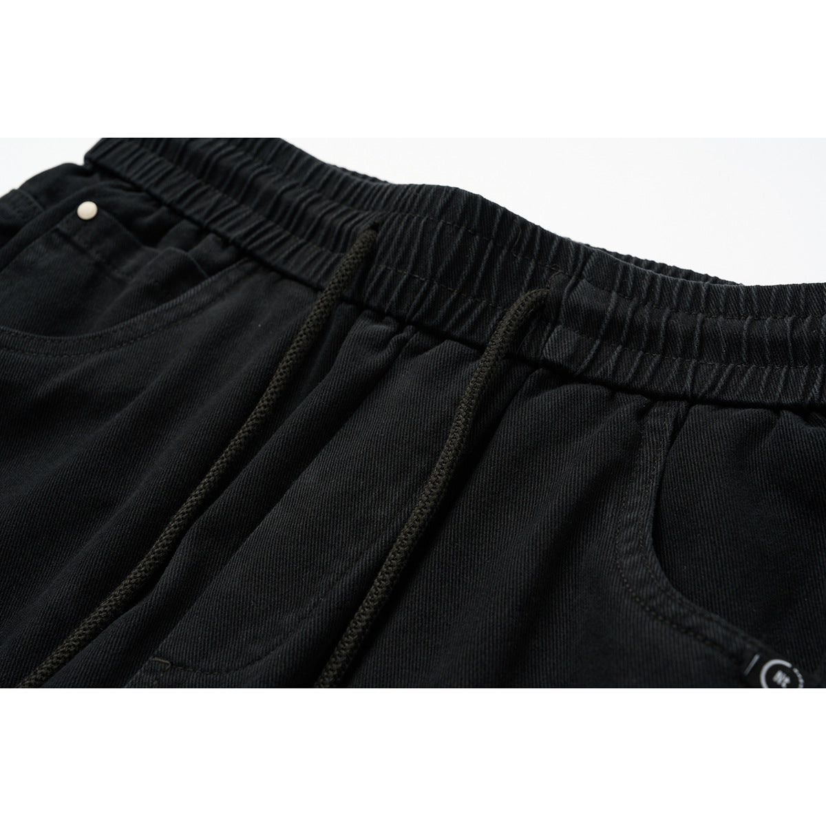 Close-up of black pants showing the elastic waistband, drawstrings, and front pockets.