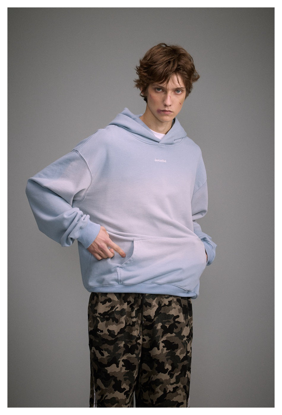 Model wearing an oversized pale blue hoodie with kangaroo pocket and small white “breathe” embroidery.